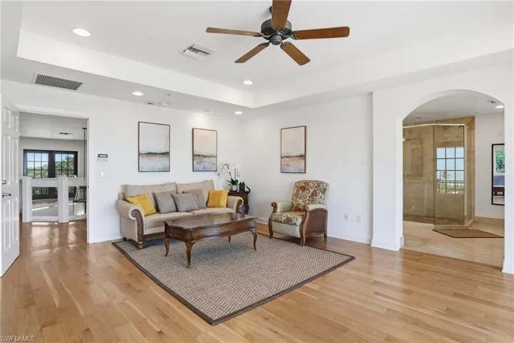Living area featuring arched walkways, a ceiling fan, light wood-style floors, a tray ceiling, and recessed lighting