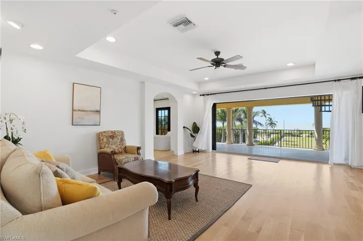 Living room with a tray ceiling, arched walkways, ceiling fan, light wood-style floors, and recessed lighting