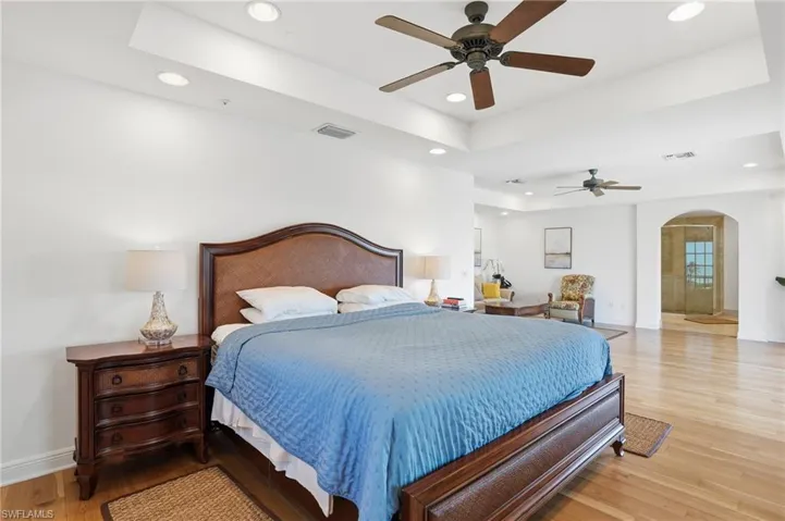 Bedroom featuring a tray ceiling, arched walkways, light wood-type flooring, a ceiling fan, and recessed lighting
