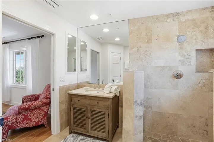 Ensuite bathroom featuring vanity, a walk in shower, tile walls, recessed lighting, and light wood-type flooring