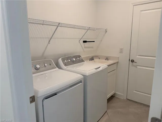 Laundry area featuring independent washer and dryer, light tile patterned floors, and cabinet space