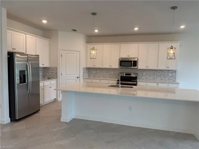 Kitchen with decorative backsplash, stainless steel appliances, white cabinets, a center island with sink, and light stone countertops