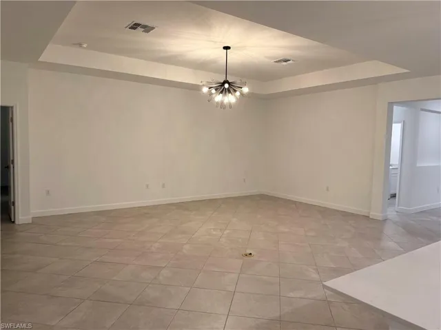 Spare room with a raised ceiling, hanging lights, and light tile patterned flooring