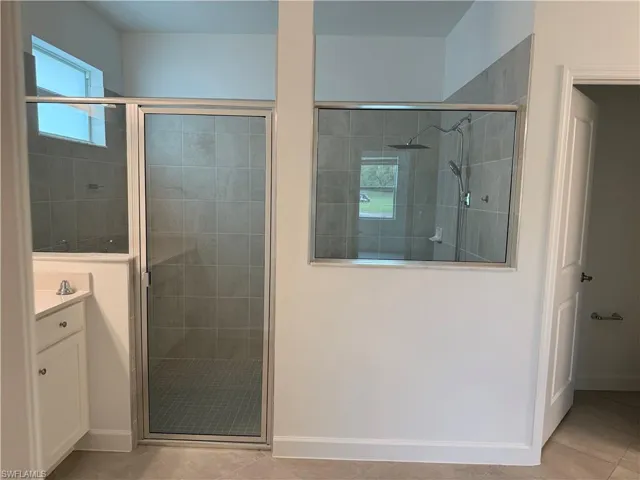 Bathroom featuring vanity, light tile patterned floors, a shower stall, and healthy amount of natural light