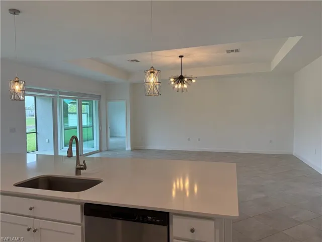 Kitchen with a raised ceiling, white cabinets, stainless steel dishwasher, open floor plan, and light stone counters