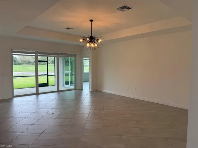Empty room featuring a tray ceiling, tile patterned floors, and suspended lighting