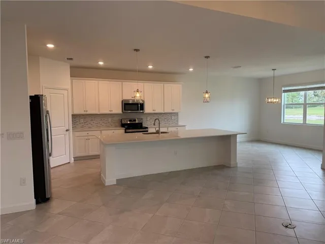 Kitchen featuring white cabinets, decorative light fixtures, a kitchen island with sink, and stainless steel appliances