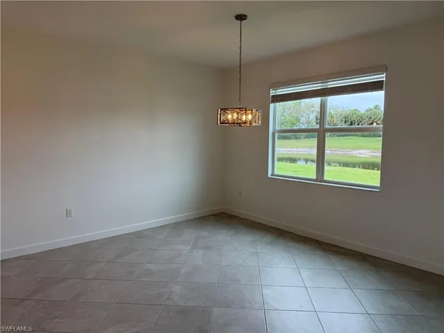 Empty room with a water view, light tile patterned floors, and hanging lights