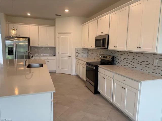 Kitchen with stainless steel appliances, white cabinetry, hanging light fixtures, and backsplash