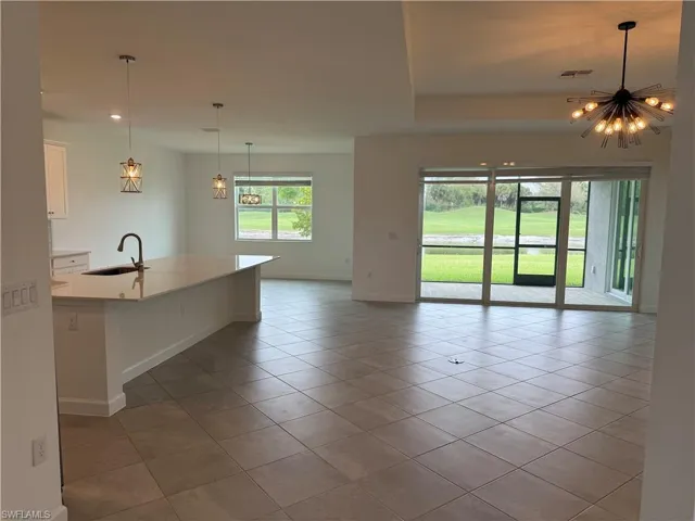 Kitchen with white cabinets, a center island with sink, a chandelier, light stone countertops, and light tile patterned floors