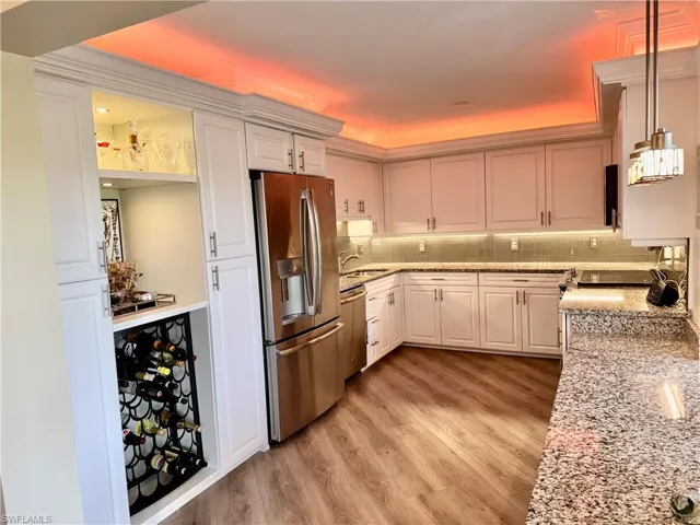 Kitchen with pendant lighting, white cabinets, appliances with stainless steel finishes, decorative backsplash, and light stone counters