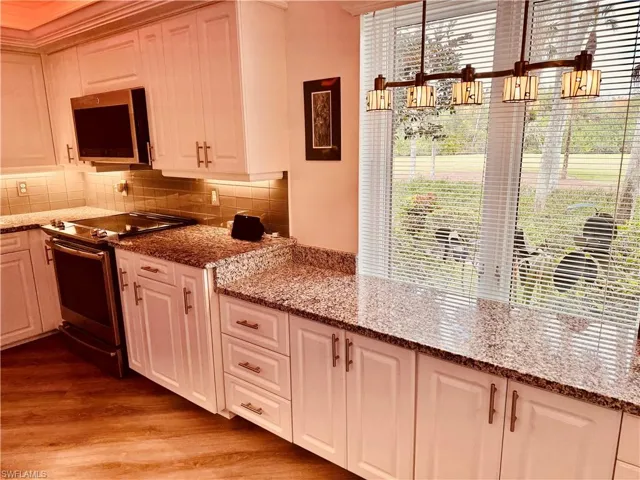 Kitchen with light hardwood / wood-style floors, appliances with stainless steel finishes, and stone counters