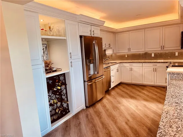 Kitchen featuring light stone countertops, stainless steel appliances, sink, backsplash, and light hardwood / wood-style flooring