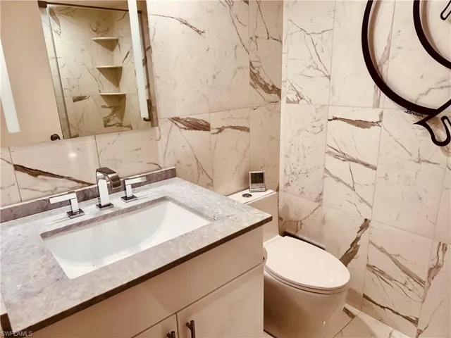 Bathroom featuring toilet, tile walls, and vanity
