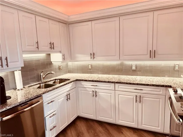 Kitchen with tasteful backsplash, sink, light stone countertops, appliances with stainless steel finishes, and dark hardwood / wood-style flooring