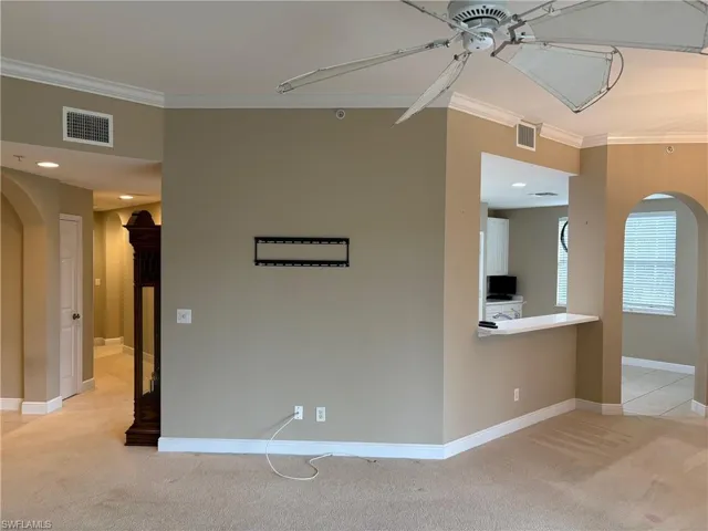 Empty room featuring arched walkways, light colored carpet, crown molding, a ceiling fan, and recessed lighting