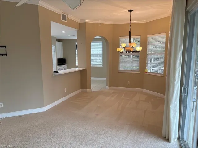 Unfurnished dining area featuring light colored carpet, crown molding, a chandelier, plenty of natural light, and arched walkways
