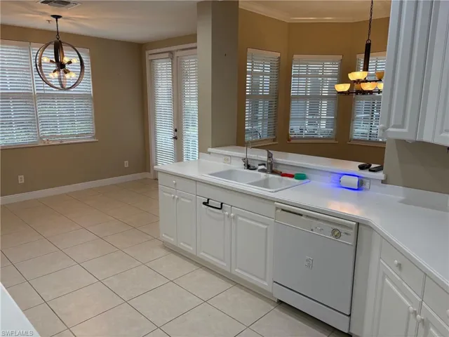 Kitchen featuring a chandelier, light countertops, white dishwasher, white cabinetry, and crown molding