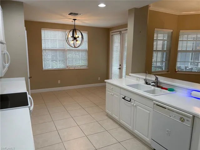 Kitchen featuring light countertops, white appliances, white cabinetry, pendant lighting, and light tile patterned floors