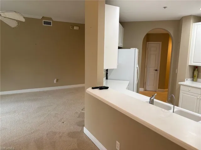 Kitchen with white cabinetry, freestanding refrigerator, ornamental molding, light carpet, and arched walkways