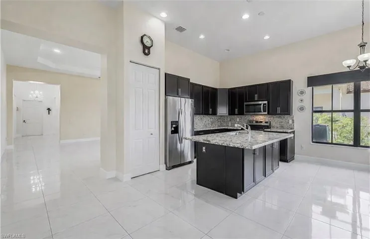 Kitchen featuring hanging lights, dark cabinetry, stainless steel appliances, and light stone countertops