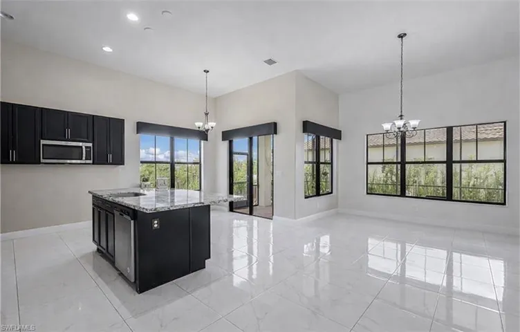 Kitchen featuring dark cabinets, suspended lighting, light stone countertops, and a high ceiling