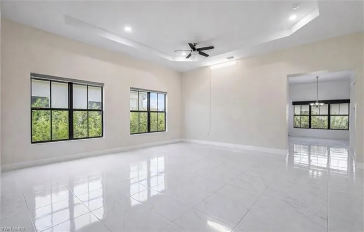 Empty room featuring a ceiling fan, a tray ceiling, and suspended lighting