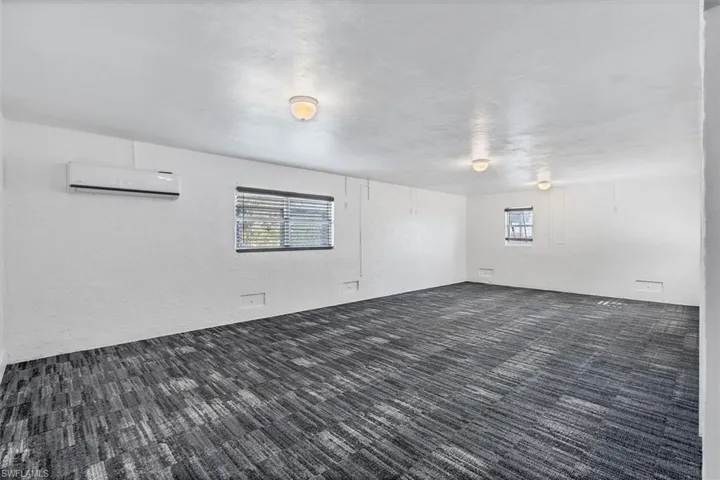 Spare room featuring a wall mounted air conditioner and dark colored carpet