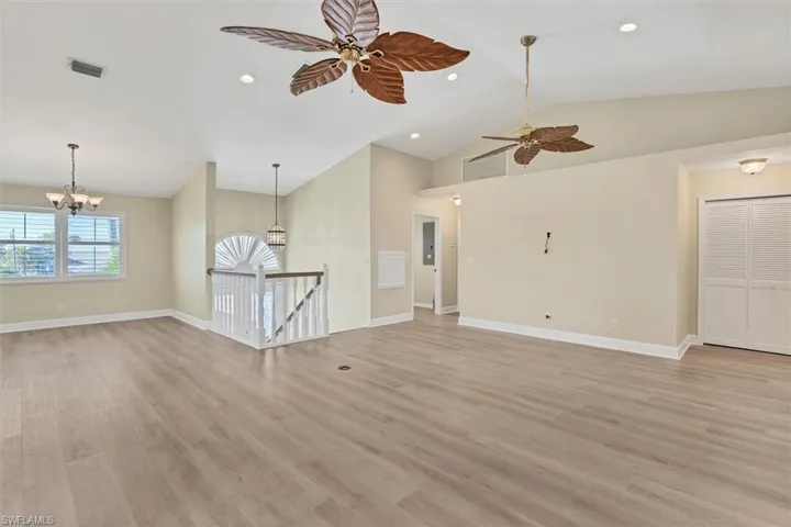 Unfurnished living room with ceiling fan with notable chandelier, electric panel, light hardwood / wood-style flooring, and lofted ceiling