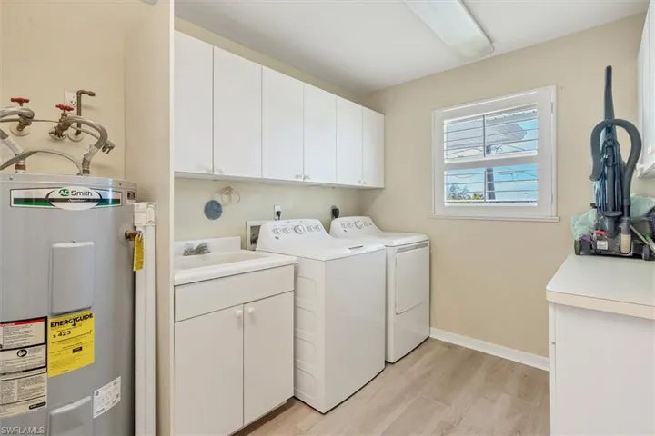 Laundry area with sink, cabinets, separate washer and dryer, electric water heater, and light hardwood / wood-style floors