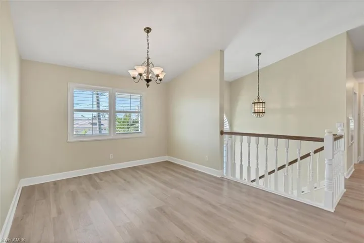 Spare room featuring vaulted ceiling, light wood-type flooring, and a chandelier