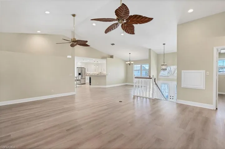 Unfurnished living room featuring ceiling fan with notable chandelier, light wood-type flooring, and high vaulted ceiling