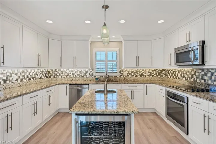 Kitchen featuring hanging light fixtures, decorative backsplash, light stone counters, stainless steel appliances, and beverage cooler