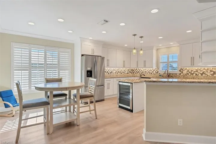 Kitchen featuring stainless steel fridge with ice dispenser, white cabinetry, light stone counters, and pendant lighting