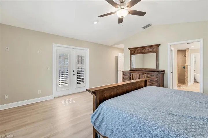 Bedroom featuring ensuite bathroom, access to outside, vaulted ceiling, ceiling fan, and light hardwood / wood-style flooring