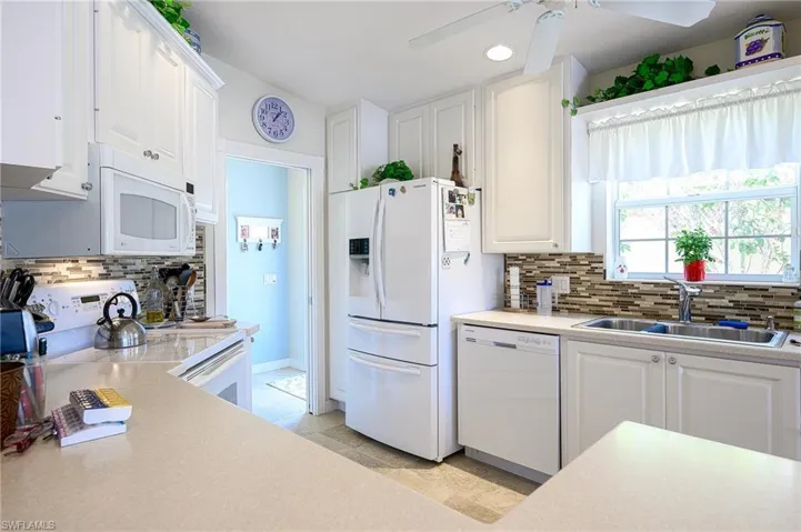 Kitchen with ceiling fan, tasteful backsplash, white appliances, sink, and white cabinets