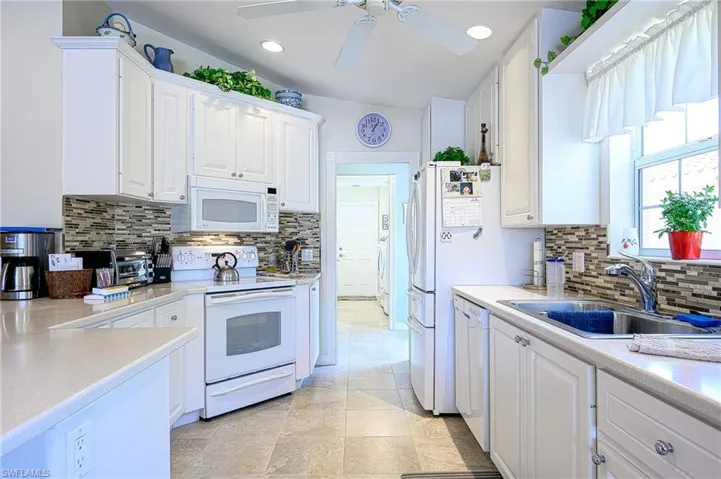 Kitchen with ceiling fan, white appliances, white cabinetry, and backsplash