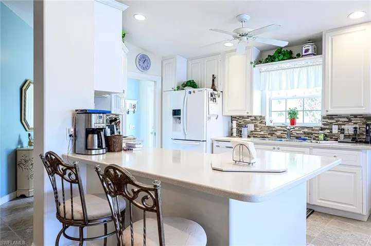 Kitchen featuring ceiling fan, light tile flooring, white refrigerator with ice dispenser and tasteful backsplash