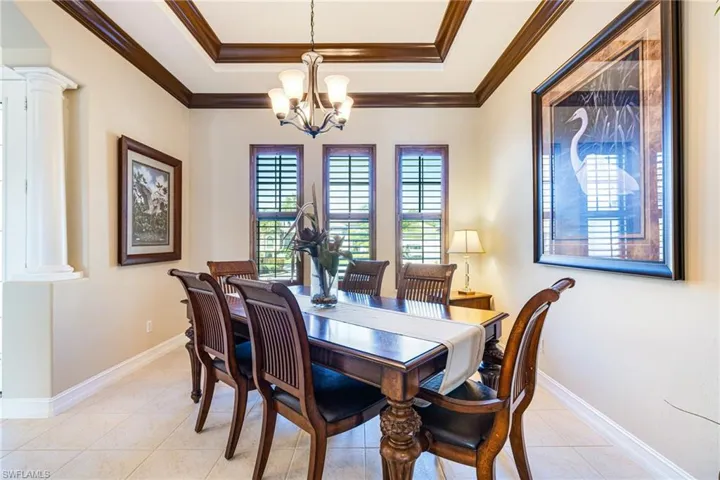 Dining area with a tray ceiling, a chandelier, ornate columns, and crown molding