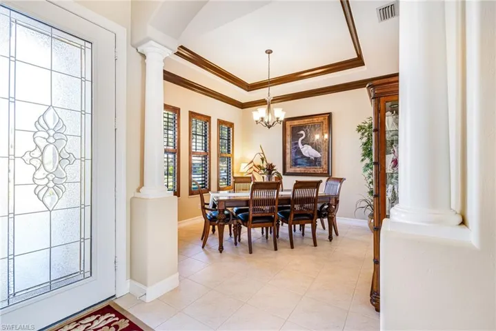 Dining room featuring ornate columns, a raised ceiling, crown molding, light tile patterned floors, and hanging lights