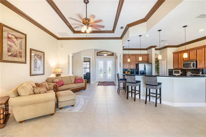 Living room featuring arched walkways, french doors, light tile patterned flooring, a ceiling fan, and crown molding