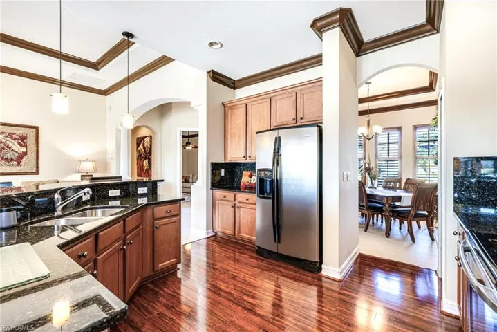 Kitchen with arched walkways, granite countertops, stainless steel appliances, decorative light fixtures, and wood-style flooring