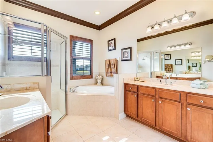 Bathroom featuring two vanities, a shower & soaking tub, crown molding, and light tile patterned floors