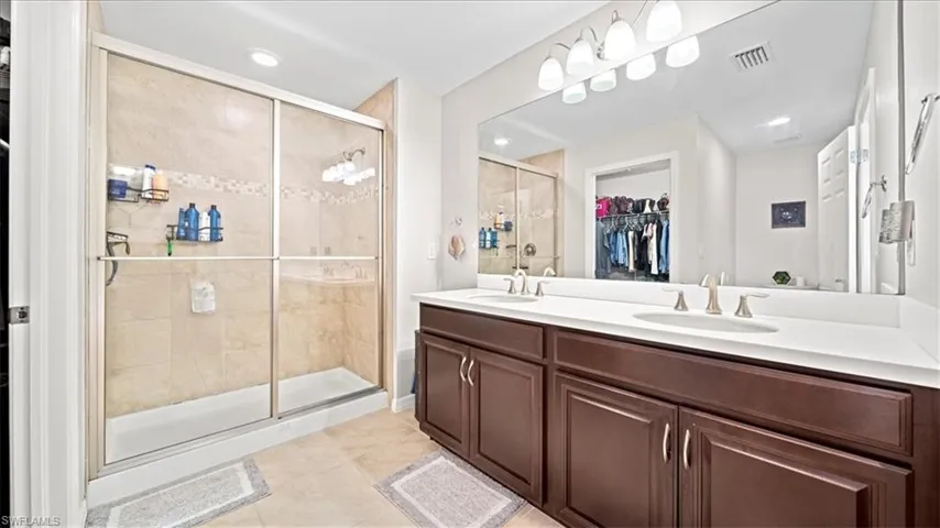 Full bath with a walk in closet, a shower stall, double vanity, light tile patterned floors, and recessed lighting