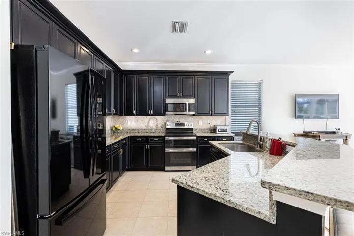 Kitchen with light tile flooring, backsplash, light stone countertops, appliances with stainless steel finishes, and sink