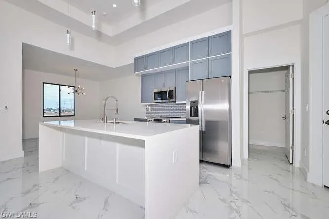 Kitchen with appliances with stainless steel finishes, a center island with sink, pendant lighting, tasteful backsplash, and light marble finish flooring