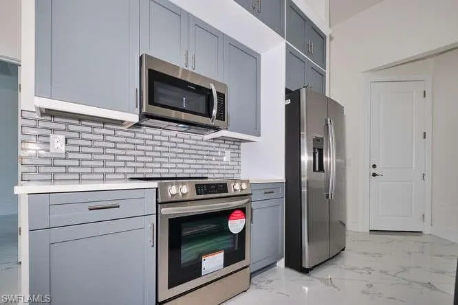 Kitchen featuring appliances with stainless steel finishes, light marble finish flooring, gray cabinetry, and backsplash