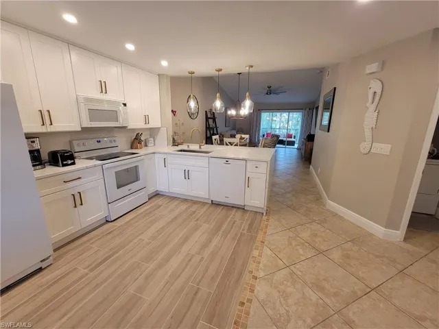 Kitchen featuring kitchen peninsula, white appliances, decorative light fixtures, sink, and white cabinets