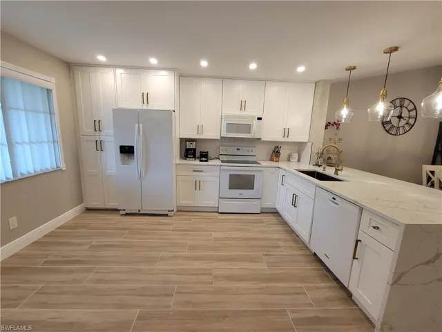 Kitchen featuring white appliances, kitchen peninsula, light stone counters, pendant lighting, and sink
