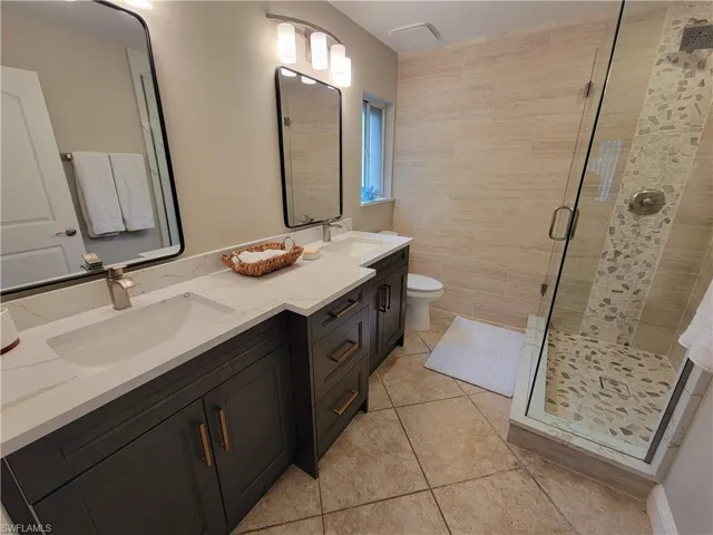 Bathroom with vanity with extensive cabinet space, dual sinks, tile floors, and a shower with door